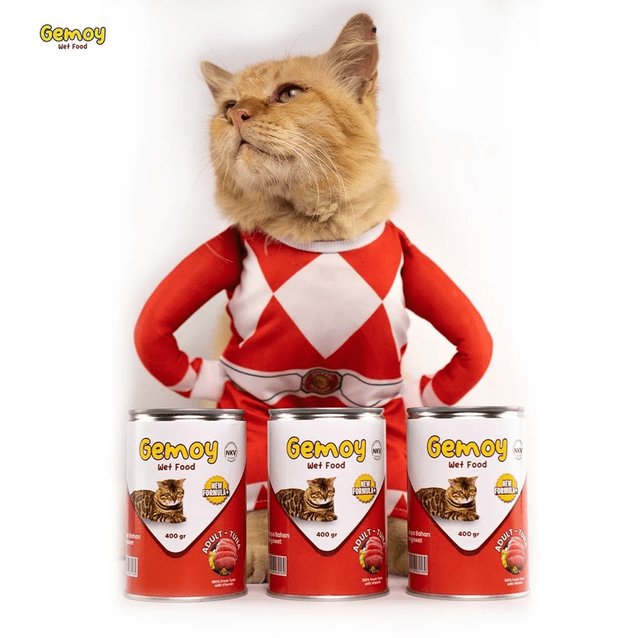 Kucing oranye berkostum merah duduk di belakang tiga kaleng Gemoy Wet Food rasa tuna